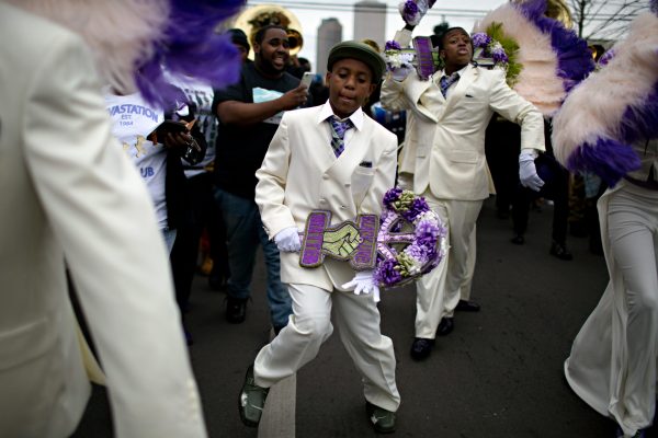 Holding a fan showing the Black Lives Matter logo, a young member of the Devastation Social Aid and Pleasure Club dances along during the Second Line Parade.